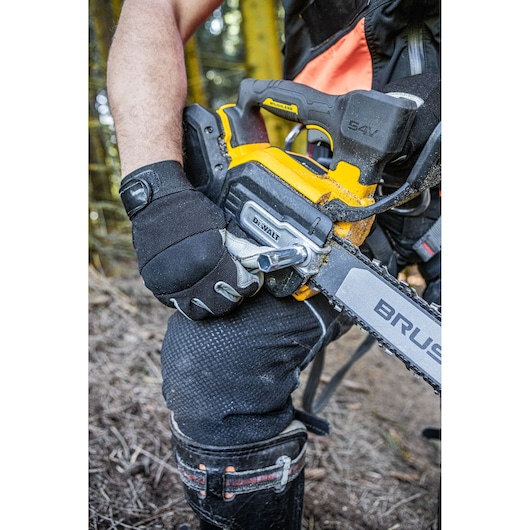 A person wearing protective gloves operates a DEWALT 54V cordless chainsaw outdoors, with the chainsaw labeled 'BRUSHLESS' and visible forest background.