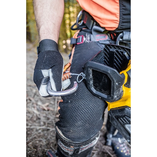 Close-up of a person wearing protective gear and gloves, holding a carabiner attached to a DEWALT power tool outdoors.