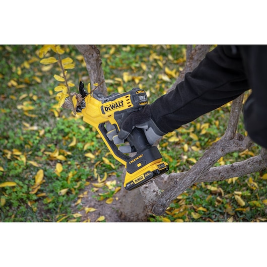 A person uses a DEWALT cordless pruning saw to cut a tree branch outdoors.