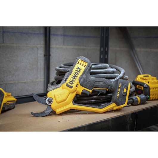 DEWALT 18V cordless pruner tool resting on a workbench, next to coiled hose and other equipment.