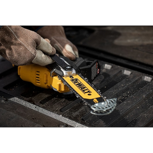 Close-up of a person wearing gloves adjusting the chain on a DEWALT cordless chainsaw placed on a truck bed.