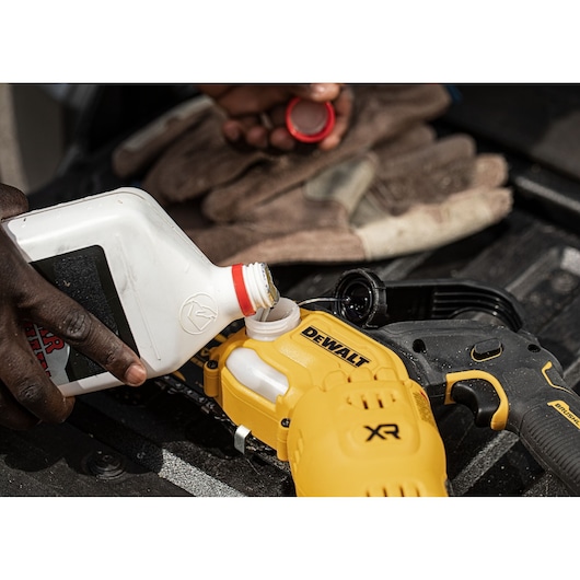 A person pours liquid from a white bottle into the oil reservoir of a yellow DEWALT XR power tool, with gloves visible in the background.