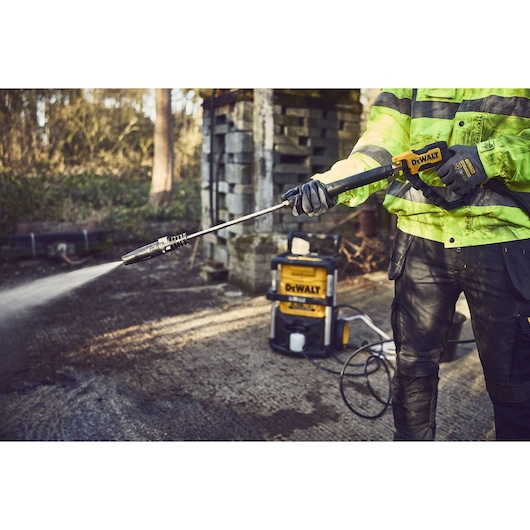 A person uses a DEWALT cordless pressure washer outdoors, spraying water on the ground.