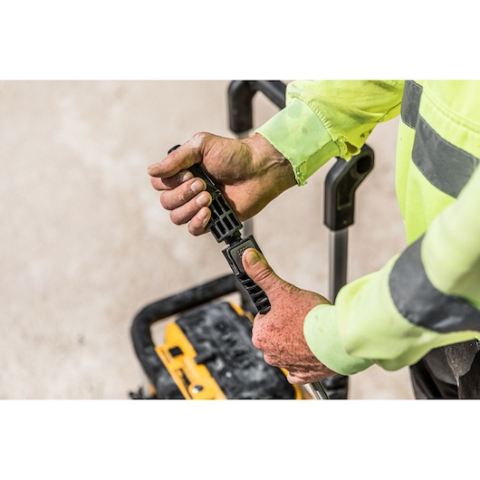 Close-up of a person wearing a high-visibility work jacket adjusting the handle of a DEWALT portable pressure washer.