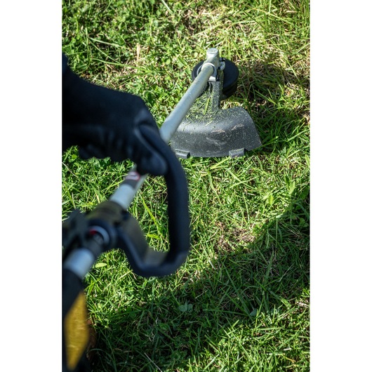 Close-up of a person using a DEWALT string trimmer to cut grass outdoors.