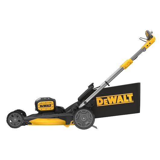 Side view of a DEWALT cordless lawn mower with black and yellow design, featuring a battery compartment and a handle extended upwards. The grass collection bag displays the DEWALT logo in yellow.