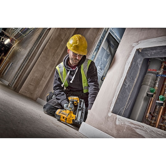 Worker using a DEWALT DCN660N nailer on a construction site, wearing a yellow hard hat and safety vest.