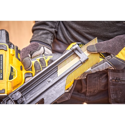 Close-up of a person wearing gloves loading nails into a yellow DEWALT 18V XR Brushless nail gun.