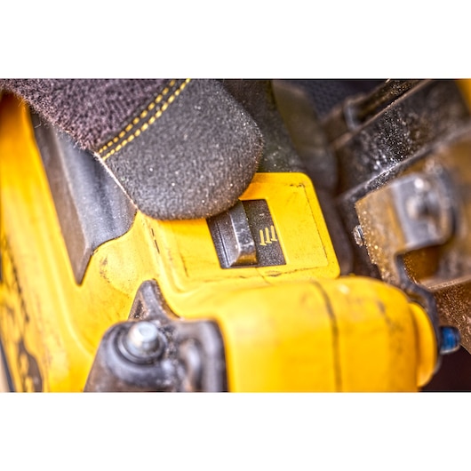 Close-up of a gloved hand adjusting a yellow DEWALT power tool switch, showing detail of the tool surface and switch markings.
