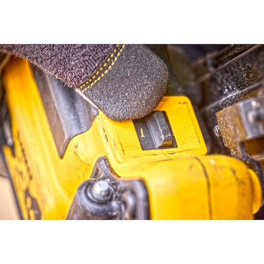 Close-up of a gloved hand adjusting a switch on a yellow DEWALT tool, with visible dust and textured surfaces.