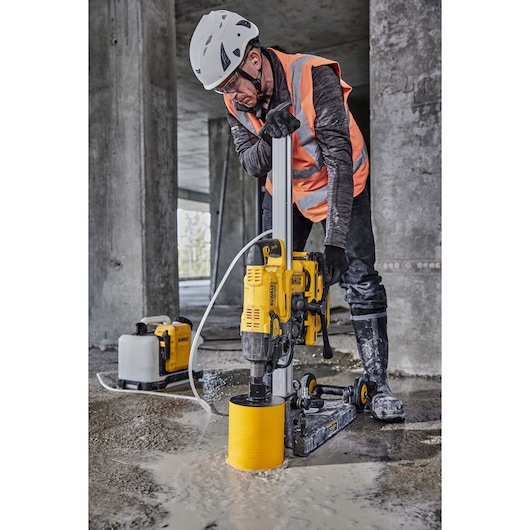 A worker uses a DEWALT DCPS151 core drill on a wet concrete floor at a construction site.