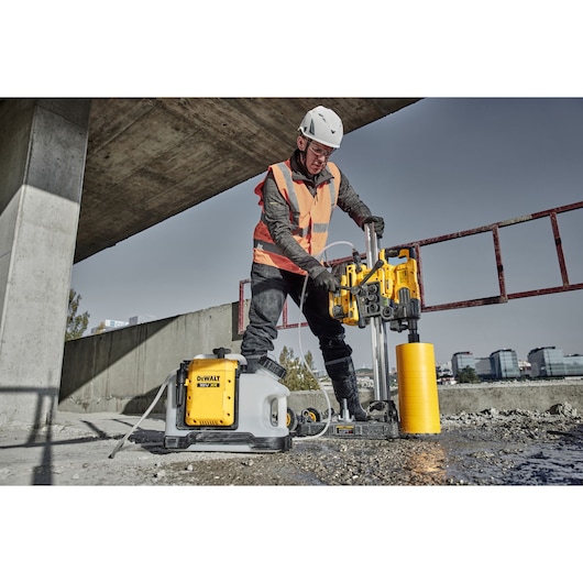 Worker uses DEWALT DCPS151 core drill on concrete at construction site, wearing safety helmet and vest.