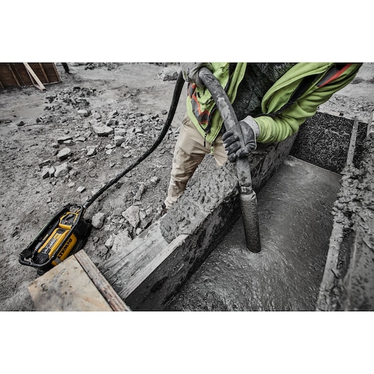 A construction worker using a DEWALT concrete vibrator tool to consolidate concrete in a foundation form at a construction site.