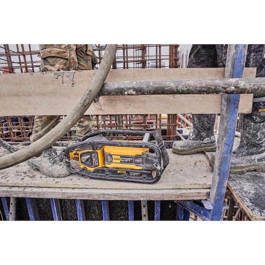 A DEWALT Power Shift cordless tool placed on a construction site platform, surrounded by workers' legs and construction materials, with concrete and rebar visible.