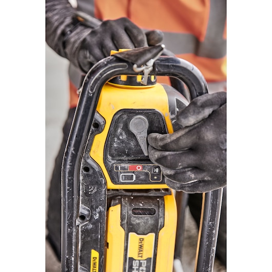 Close-up of a person wearing black gloves operating a DEWALT power tool, with focus on the control panel and battery compartment.