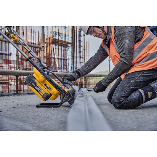 A person wearing construction safety gear uses a DEWALT cordless power tool (SKU: DCPS330N) on a metal beam at a construction site.