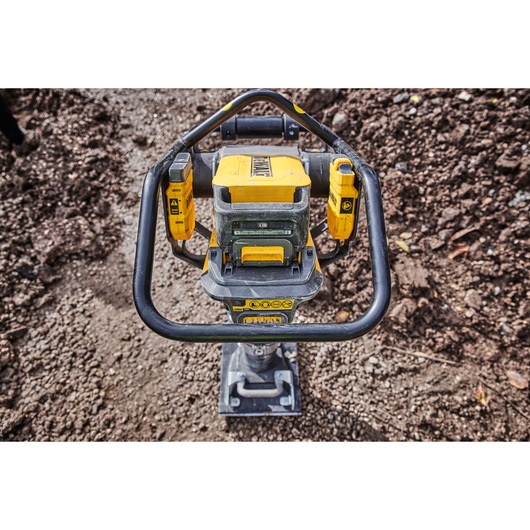 A DEWALT battery-powered compactor standing on a gravel surface outdoors, shown from above with visible handle and control panel.