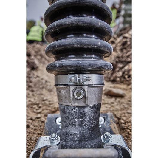 Close-up view of a DEWALT power tool component with a coiled spring and metal fittings, positioned on a construction site with soil in the background.