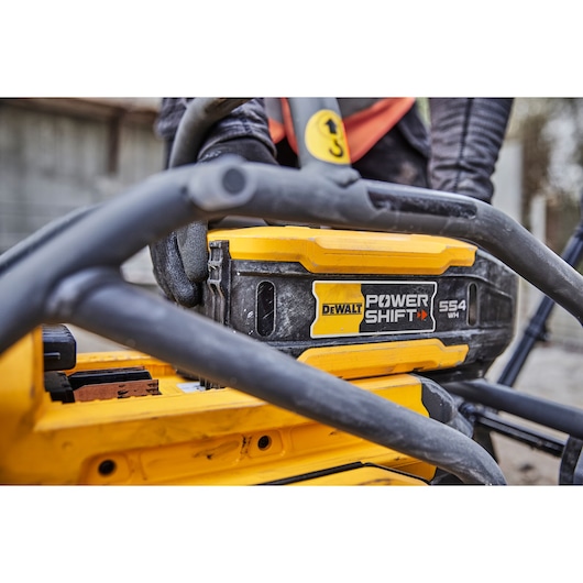 Close-up of a DEWALT Power Shift 554 Wh battery installed in a yellow DEWALT tool, with a gloved hand operating it outdoors.