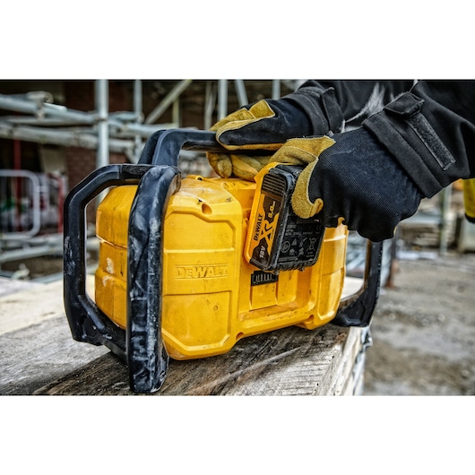 A close-up of a DEWALT portable radio with a battery being inserted by a person wearing gloves at a construction site.
