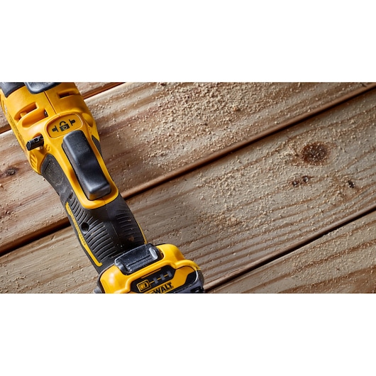 Close-up of a DEWALT cordless power tool placed on wooden planks, with sawdust scattered around.