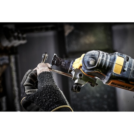 Gloved hand uses a DEWALT oscillating tool to cut metal in a workshop.