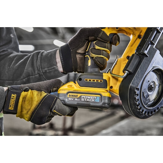 Close-up of a DEWALT 18V POWERSTACK cordless bandsaw being operated by a person wearing protective gloves, with focus on the battery and handle.