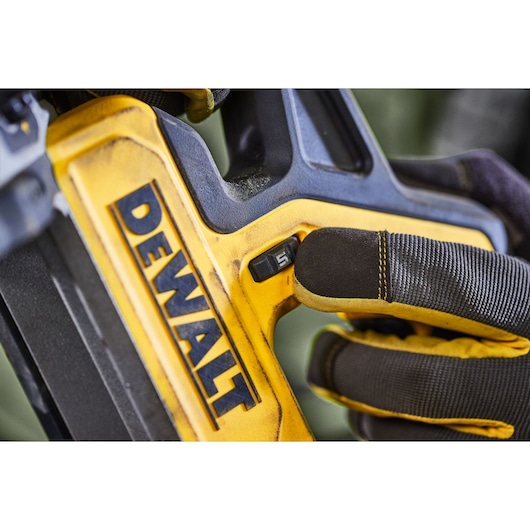 Close-up of a gloved hand adjusting a switch on a yellow DEWALT power tool.