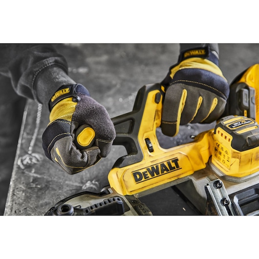 Close-up of hands wearing protective gloves operating a DEWALT cordless power tool with a yellow and black handle on a workshop table.