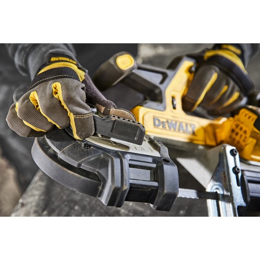 Close-up of gloved hands adjusting a DEWALT cordless band saw tool. The tool features a yellow and black design and is being prepared for use in a workshop setting.