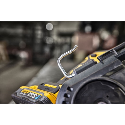 Close-up view of a DEWALT cordless tool, showing a metal hook attachment and part of the POWERSTACK battery pack.
