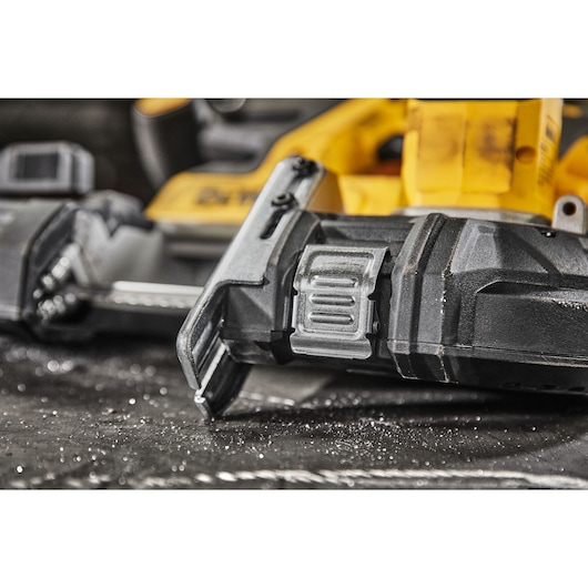 Close-up image of a DEWALT handheld power tool, specifically focusing on the blade and the adjustment mechanism, resting on a work surface with metal shavings.