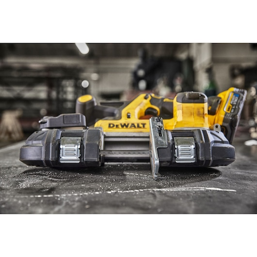 A close-up view of a DEWALT cordless band saw placed on a workbench in an industrial workshop setting.
