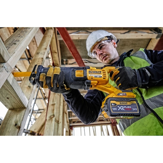Worker using a DEWALT DCS389N cordless reciprocating saw on wood at a construction site.