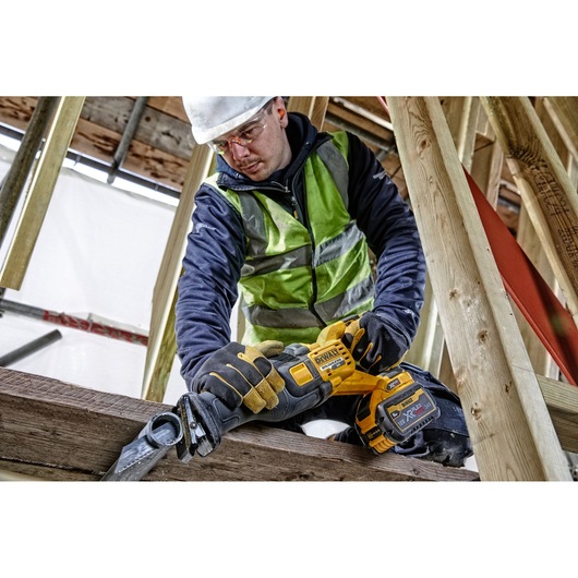 Worker uses DEWALT DCS389N cordless saw to cut wood at construction site, wearing safety gear.