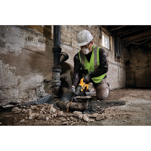 Worker using DEWALT tool to cut a pipe in a construction site with rubble on the floor.