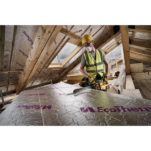 Worker uses DEWALT saw to cut EcoTherm insulation board in a roof attic, wearing safety gear and high-vis vest.