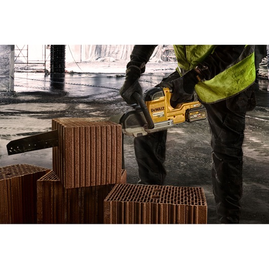 Worker uses a DEWALT cordless saw to cut a red construction block on a worksite.