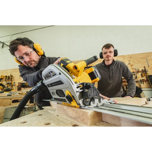 Man using a DEWALT track saw to cut wood, with another person observing in a workshop.