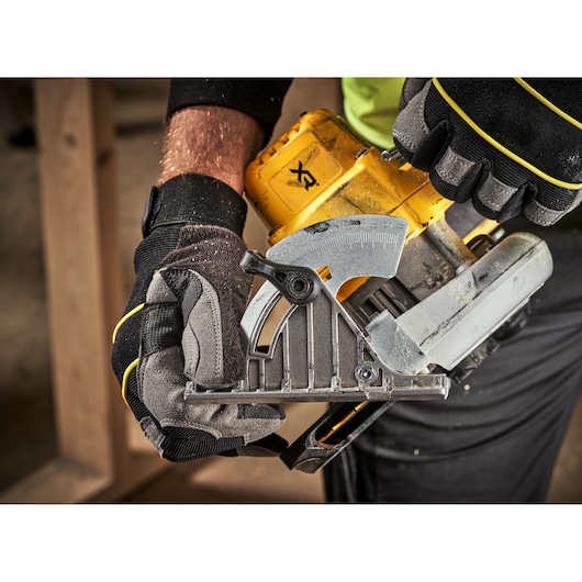 Close-up of gloved hands adjusting the angle setting on a DEWALT cordless circular saw during woodworking.