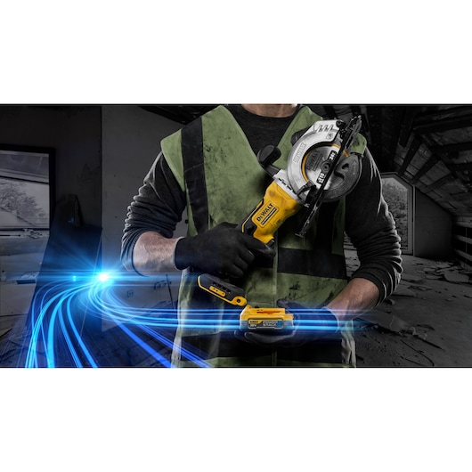 Person wearing a safety vest and gloves holding a DEWALT cordless circular saw, model DCS571, in a dimly lit construction or renovation site with blue light streak effects.