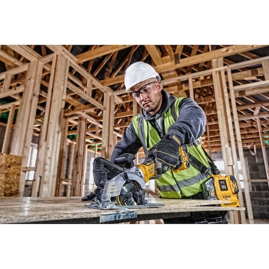 Worker uses a DEWALT DCS571N cordless saw to cut wood on a construction site with timber framing.