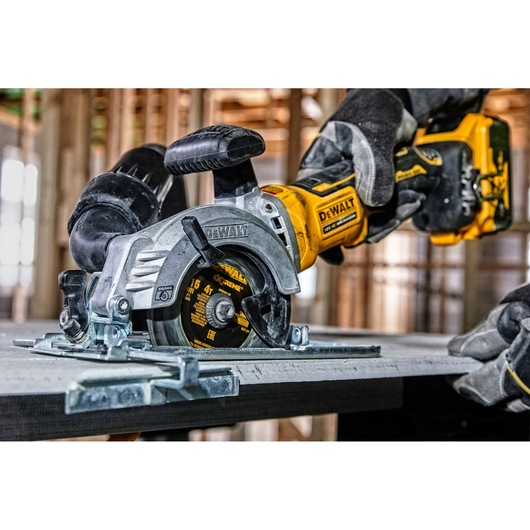 DEWALT cordless circular saw DCS571N cutting wood, operated by gloved hands at a construction site.