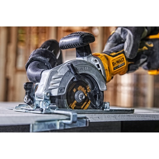DEWALT cordless circular saw in use, cutting a material sheet on a workbench in a workshop setting.