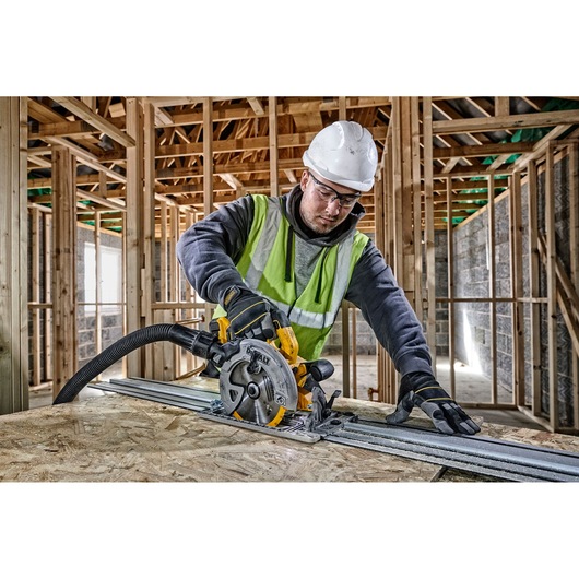 Worker uses DEWALT circular saw to cut wood on construction site, wearing safety gear.