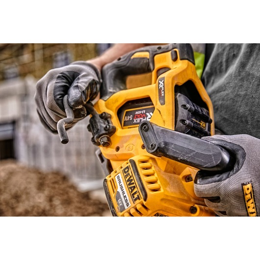Close-up of gloved hands holding a yellow DEWALT cordless circular saw on a construction site.