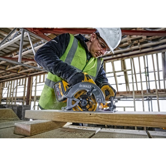 Worker using DEWALT DCS578NT circular saw to cut wood at a construction site.