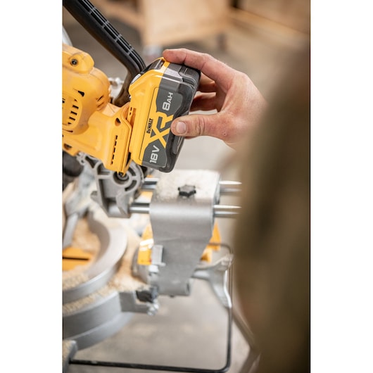 Close-up of a person installing an 18V XR battery onto a yellow DEWALT power tool in a workshop setting.