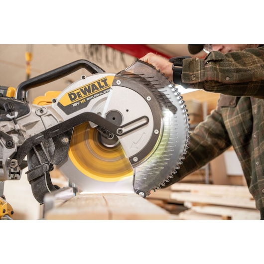 A close-up of a person using a DEWALT 18V XR brushless mitre saw to cut a piece of wood in a workshop setting.