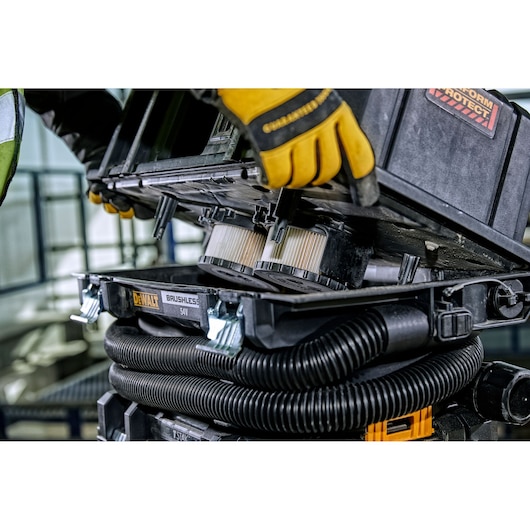 Close-up of a person wearing yellow gloves while opening the DEWALT DCV586MT2 54V brushless vacuum cleaner to show the internal filters and hose.